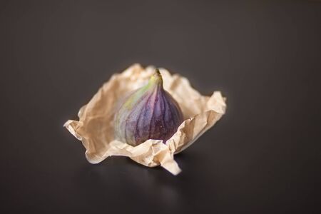 Lone figs in craft packaging on a black background