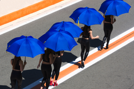 Women with umbrellas to shelter from the sun walk following lines drawn on the asphaltの写真素材