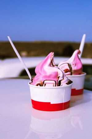 Two tubs of strawberry ice cream and fresh cream served on the roof of a car next to the beach