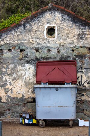 A dumpster next to an old house facade with a small window that looks like ruins