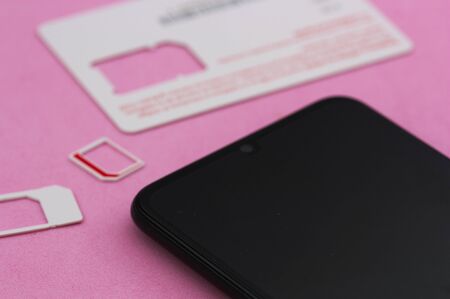Some mobile phone cards (sim cards) next to a next-generation smart phone on a pink background.の写真素材