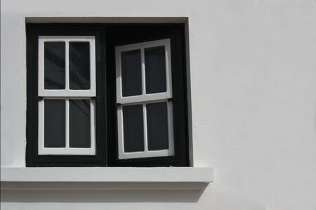 A half-open window of wood and black-painted glass on a rough white wall with space to add texts to...