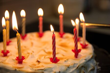 Anniversary celebration cake in which wax candles are being lit with the help of a lighter