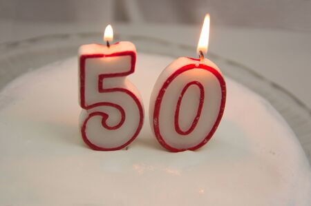 Burning red and white candles that form the number fifty on a cake decorated with white meringue
