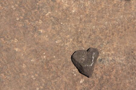 A heart-shaped stone on a textured brown stone surface with space for texts, copy spaceの写真素材