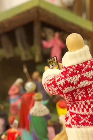 A wooden doll dressed in a Christmas sweater photographs the main scene of a traditional birth of...