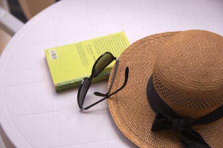 On a table we see a straw hat, sunglasses and a reading book spending free time in summerの写真素材