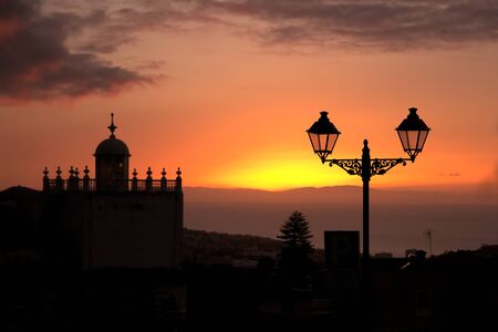 Sunset over the city of Orotava with the silhouette of a lamppost and the tower of a city churchの写真素材
