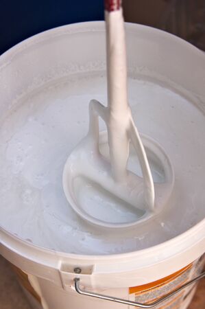 Someone removes the contents of a bucket of white paint with a paint shakerの写真素材