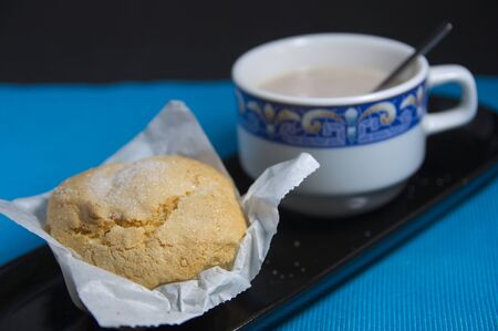 Cup of cocoa with milk with an accompanying cupcake served all in a black ceramic tray on a blue...
