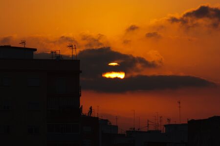 Landscape of a city where you can see the profile of modern buildings with television antennas while the sun falls between the clouds in the backgroundの写真素材