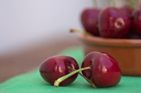 Cherries with their stems crossed on a green table and a blurred bowl in the background and space...