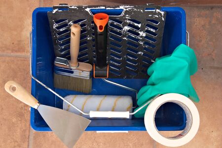 Top view of a paint bucket in which there is a painter's brush and roller, along with gloves and a...