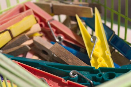 Multi-colored plastic clothespins mixed together with other wooden clothespins in a green basket