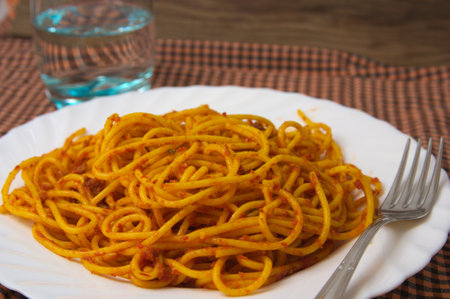 Closeup of a table served with silverware and glass of water next to a plate of spaghetti with tomatoのeditorial素材