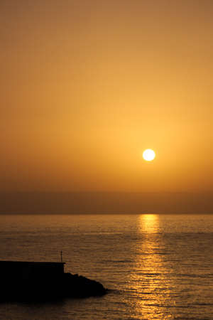 Vertical image of a sunrise near a sea port in which the orange colors of the sunlight stand out
