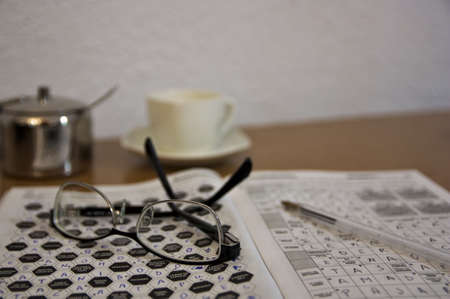 Close-up of some reading glasses and some crosswords that someone does as a hobby while having a coffeeの写真素材