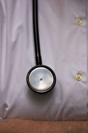 Close up of a stethoscope hanging over a white button down shirt that is part of a doctor's uniformの写真素材