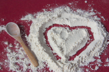 Kneading table in which a heart has been drawn on a pile of flour next to a wooden spoon