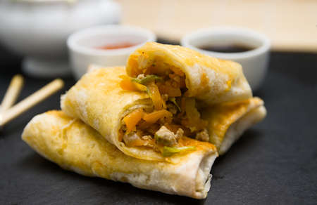 Close-up of some homemade spring rolls on a black slate plate with soy sauce, sweet and sour and...