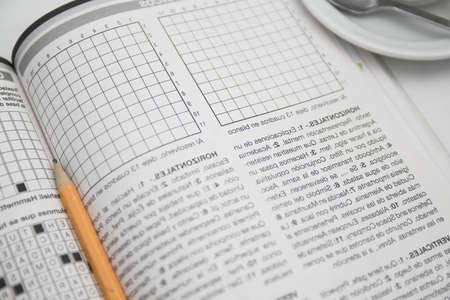 Close-up of a sheet of a puzzle book type crossword puzzles or alphabet soup, next to a cup of coffee and a pencilの写真素材