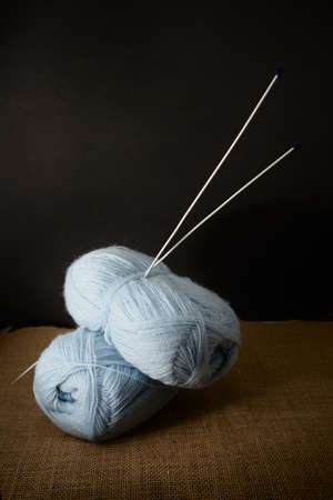 Some balls of blue yarn with the knitting needles stuck on them on a black background, copy space...
