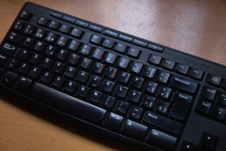 Flat lay view of a black multimedia keyboard with western characters on a wooden table