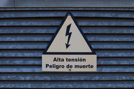 Sign on a door warning that there are high-voltage connections in that area that can endanger life. The poster is written in Spanish and its translation is: "High Voltage, Danger of death"の写真素材