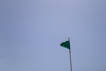 Close-up of a green flag on a beach silhouetted against the blue summer sky and symbolizing that the sea water is suitable for bathingの写真素材