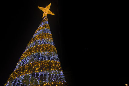 Ground view image of a Christmas tree decorated with stars and LED lights with a dark background and...