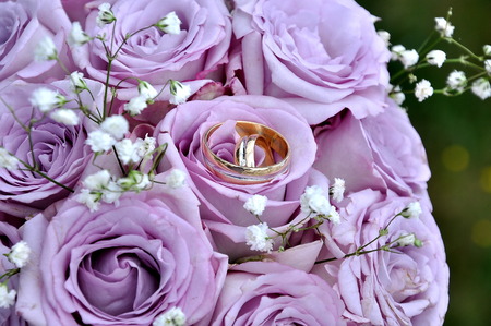 Wedding rings on a bouquet of purple rosesの写真素材