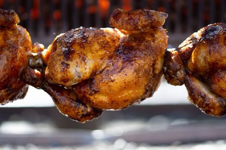 Roasted chickens on spit grilled over fire of a big barbecue,の写真素材