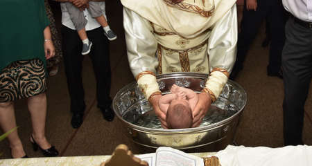 baby  baptism in Orthodox Church Romania,sinking , child in holy water during baptismの写真素材