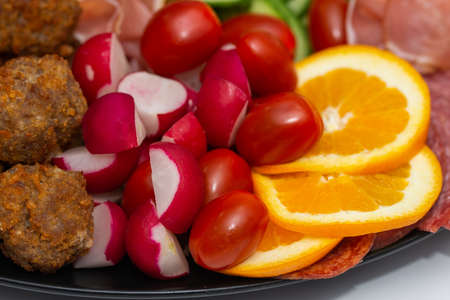 plate with vegetables and fruits., oranges, tomatoes, cheese, grapes, sausagesの写真素材