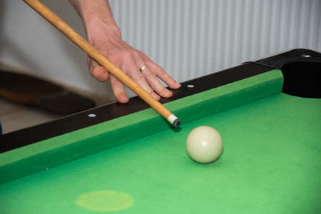 Hand with cue aiming on billiard ball at table