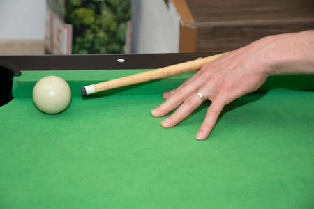 Hand with cue aiming on billiard ball at table