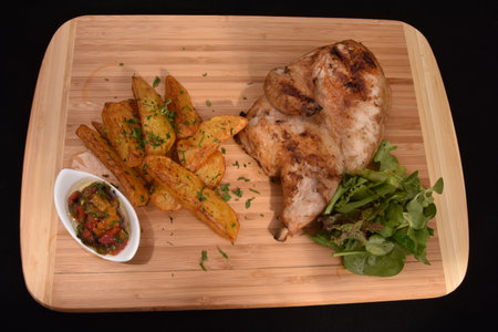culinary preparation consisting of half a grilled chicken, served with potato wedges (or French fries cut into wedges), a fresh green salad, and a sauce or salsa, possibly vegetablの写真素材