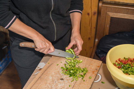 a person dicing green bell peppers on a wooden cutting board using a chef's knife. This is a common food preparation technique used in cooking for various dishes, such as stir-frieの写真素材