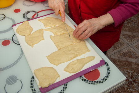 a person cutting puff pastry dough into smaller pieces on a white cutting board.