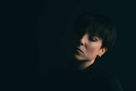 Dreamy portrait of a woman closing her eyes in studio with a black backdrop