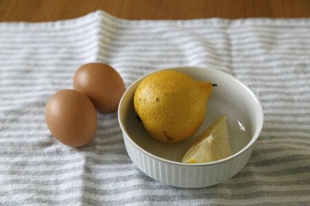 High shot of lemons inside a white bowl with 2 organic eggs aside over a dishtowel on a wooden tableの写真素材