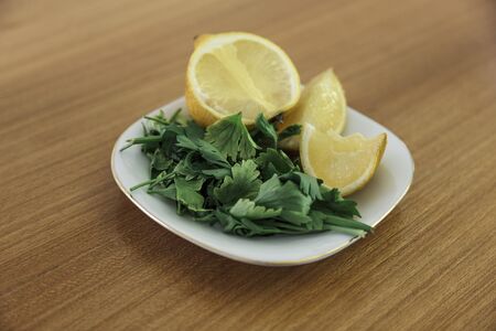 Front shot of a white plate with parsley leafs and sliced lemons on a wooden tableの写真素材