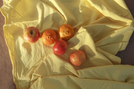 Cenital Shot of organic apples and tangerines over a yellow tablecloth on a red floorの写真素材