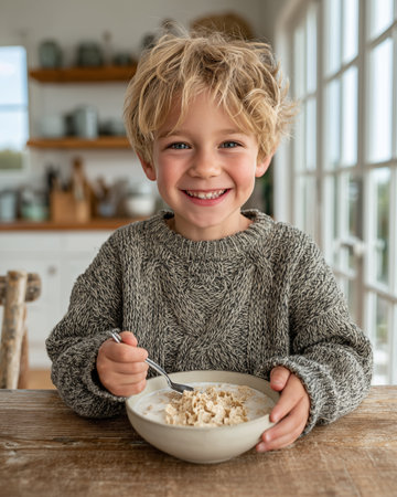 Portrait of a smiling little boy eating oatmeal in the kitchenの素材