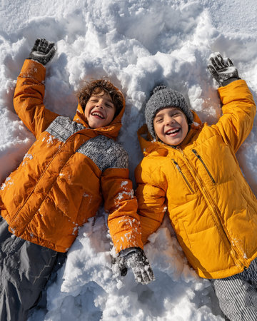 high angle view of smiling boys in warm clothes lying in fresh snowの素材