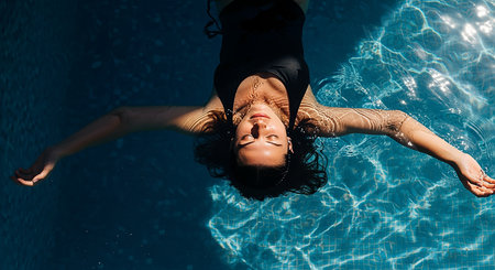 Top view of young woman in swimsuit relaxing in swimming pool.の素材