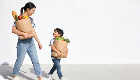 Mother and daughter carrying paper bags with fresh vegetables and fruits, healthy food conceptの素材