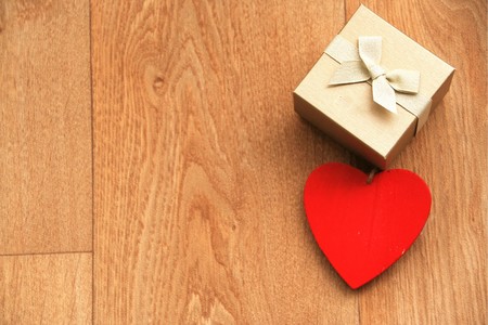 gift box with bow and a red heart hanging on a wooden table with copy - spaceの写真素材