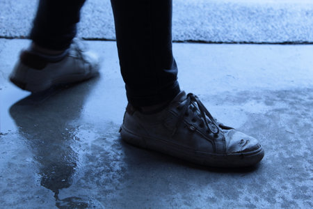 Close up of male legs in black jeans and white sneakers on concrete background.