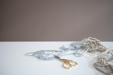 Golden scissors on white table in daylight. Loose threads, wool.の写真素材